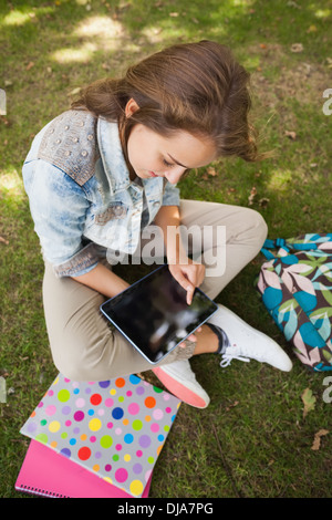 Pretty happy student sitting on grass using tablet Stock Photo