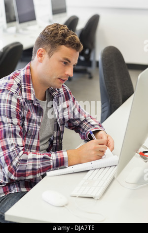 Handsome smiling student using computer taking notes Stock Photo