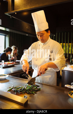 Japanese chef at work in a restaurant, chopping and cooking green vegetables on a hot plate in the open kitchen. Stock Photo