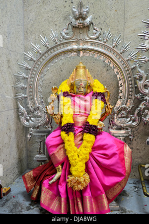 Statue of a four-armed Hindu deity, adorned with a colourful garland of yellow flowers and a pink dress. Stock Photo