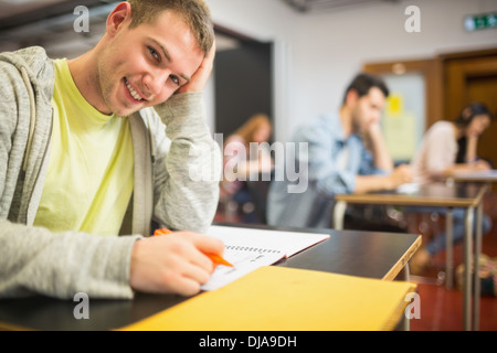 Smiling male student with others writing notes in classroom Stock Photo