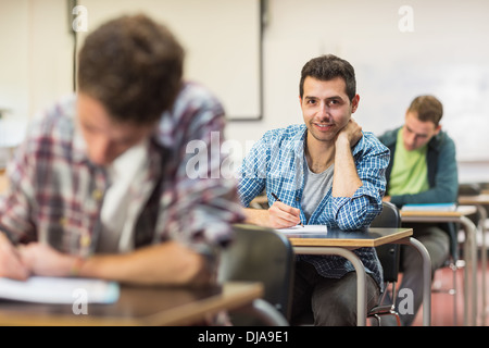 Male student with others writing notes in classroom Stock Photo