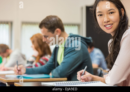 Female student with others writing notes in classroom Stock Photo
