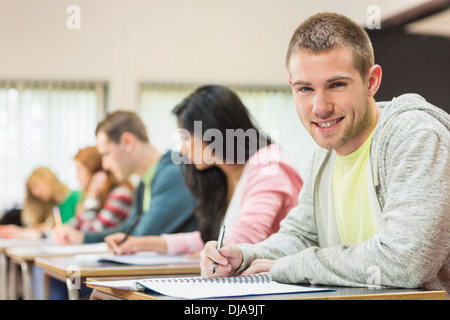 Smiling male student with others writing notes in classroom Stock Photo