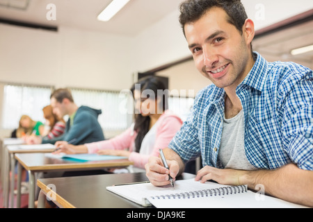Smiling male student with others writing notes in classroom Stock Photo