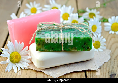 Three bars of soap pink, green and white on a piece of paper, daisy flowers on a background of wooden boards Stock Photo