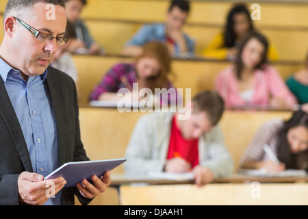 Teacher using tablet PC with students at lecture hall Stock Photo