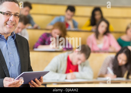 Teacher using tablet PC with students sitting at lecture hall Stock Photo