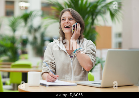 Student doing homework while on call by laptop in cafe Stock Photo
