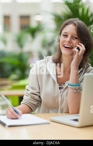 Cheerful student doing homework while on call by laptop at cafe Stock Photo
