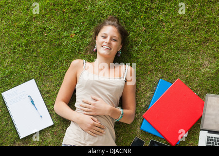 Smiling young woman lying on grass with books Stock Photo
