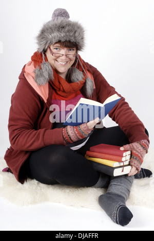 Woman in winterclothes holding a stack of books and reading aloud Stock Photo