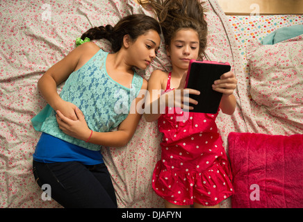 Mixed race sisters using digital tablet on bed Stock Photo