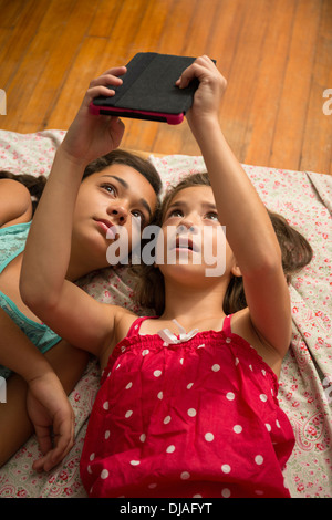 Mixed race sisters using digital tablet on bed Stock Photo
