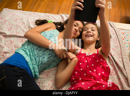 Mixed race sisters using digital tablet on bed Stock Photo