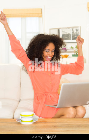 Mixed race woman cheering at laptop Stock Photo