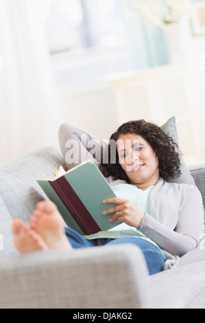 Hispanic woman reading on sofa Stock Photo