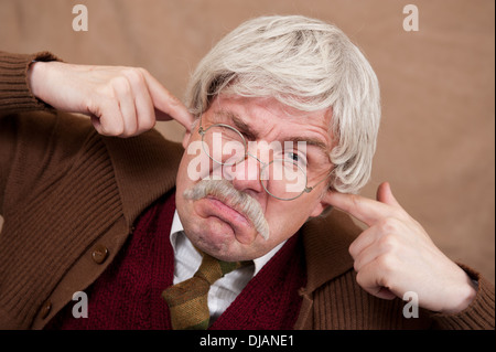 Grey haired old man trying to block out the noise by putting his fingers in his ears. Stock Photo