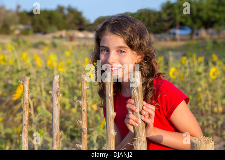 Smiling farmer girl with sunflowers field holding fence door in Mediterranean Stock Photo