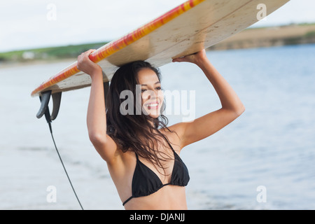 Bikini woman holding surfboard over head at beach Stock Photo