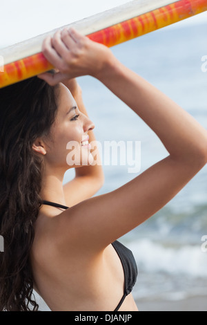 Bikini woman holding surfboard over head at beach Stock Photo