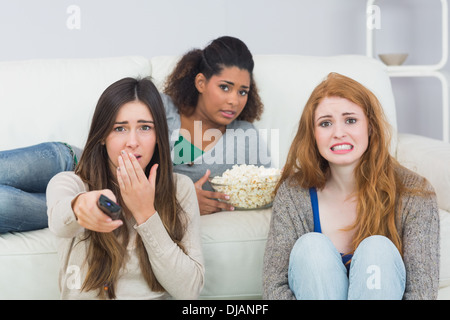 Scared friends with remote control and popcorn bowl at home Stock Photo