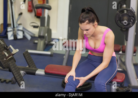 Healthy woman with an injured knee sitting in gym Stock Photo