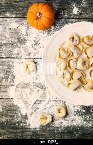 Top view on plate of homemade pasta ravioli over wooden table with flour and orange pumpkin. See series Stock Photo