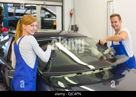 Two glaziers replace windshield or windscreen on a car in workshop after stone-chipping Stock Photo