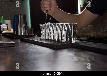 Close-up of the hand of the barman pouring liquor into shot glasses aligned on the bar, shot from low angle Stock Photo