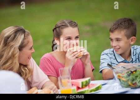 Young girl eating burger while mother and brother smiling at her Stock Photo