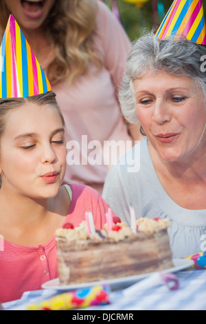 Close up of young girl and her grandmother blowing candles Stock Photo