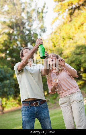 Young man opening champagne bottle with his wife Stock Photo