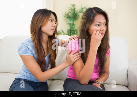 Upset woman sitting on a couch being consoled by her sister Stock Photo