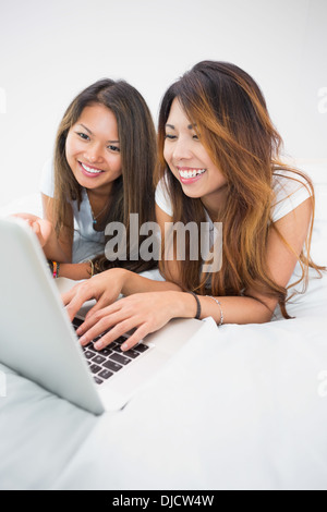 Two happy brunette sisters lying on a bed using a laptop Stock Photo