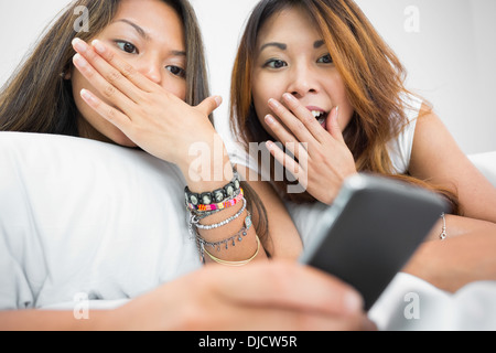 Two shocked pretty sisters using a smartphone Stock Photo