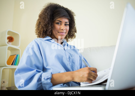 Pretty smiling student making notes and using laptop Stock Photo