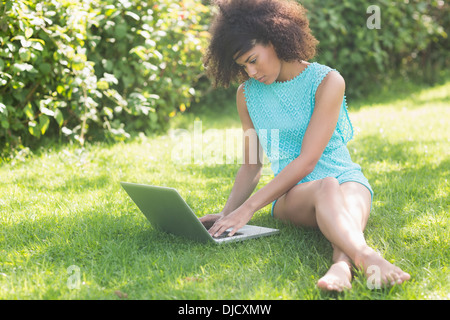 Gorgeous focused brunette sitting on grass using laptop Stock Photo