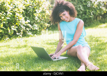 Gorgeous smiling brunette sitting on grass using laptop Stock Photo