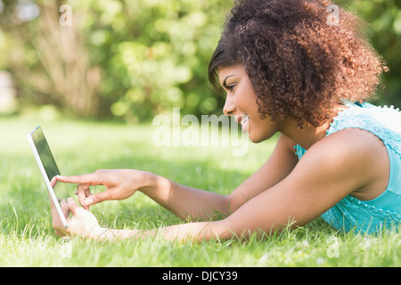 Gorgeous content brunette lying on grass using tablet Stock Photo