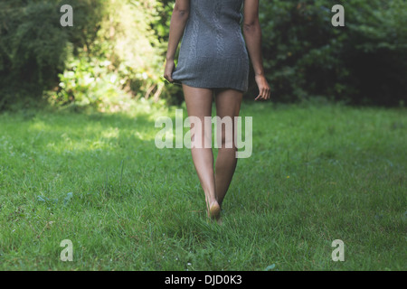 Rear view of lower body of model walking on grass holding dress Stock Photo