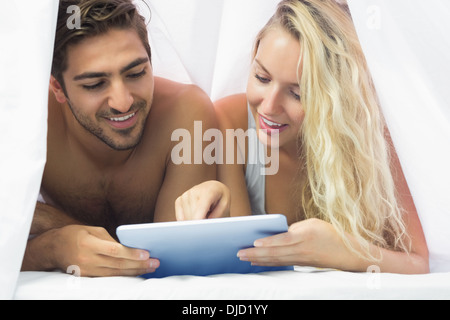Cheerful couple lying under the sheet using a tablet Stock Photo