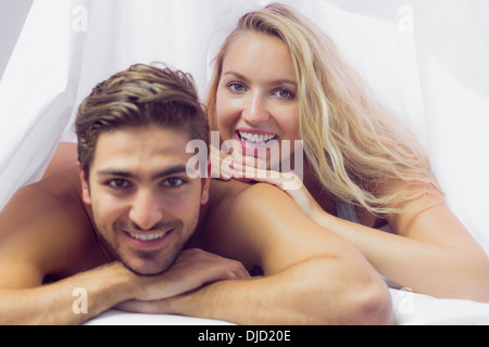 Smiling young couple lying under a blanket Stock Photo