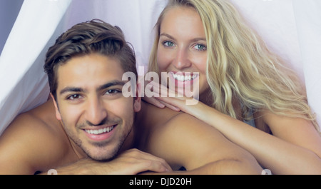 Attractive smiling couple lying under a blanket Stock Photo