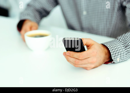 Closeup image of a male hand typing on smartphone and holding cup of coffee Stock Photo
