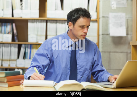 Calm librarian using a laptop and taking notes Stock Photo