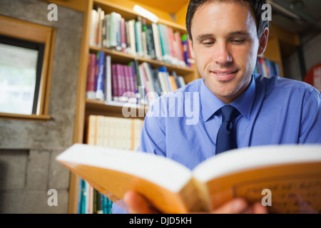 Smiling librarian sitting at desk reading a book Stock Photo