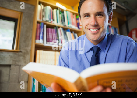 Cheerful librarian sitting at desk reading a book Stock Photo