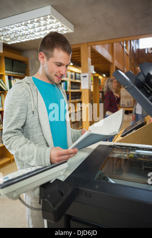 Happy good looking student standing next to photocopier Stock Photo
