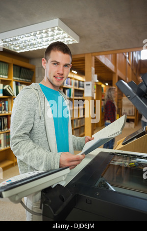 Smiling good looking student standing next to photocopier Stock Photo
